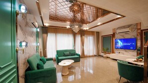 Een moderne woonkamer met een groene bank, een ronde salontafel en een flatscreen televisie aan de muur.