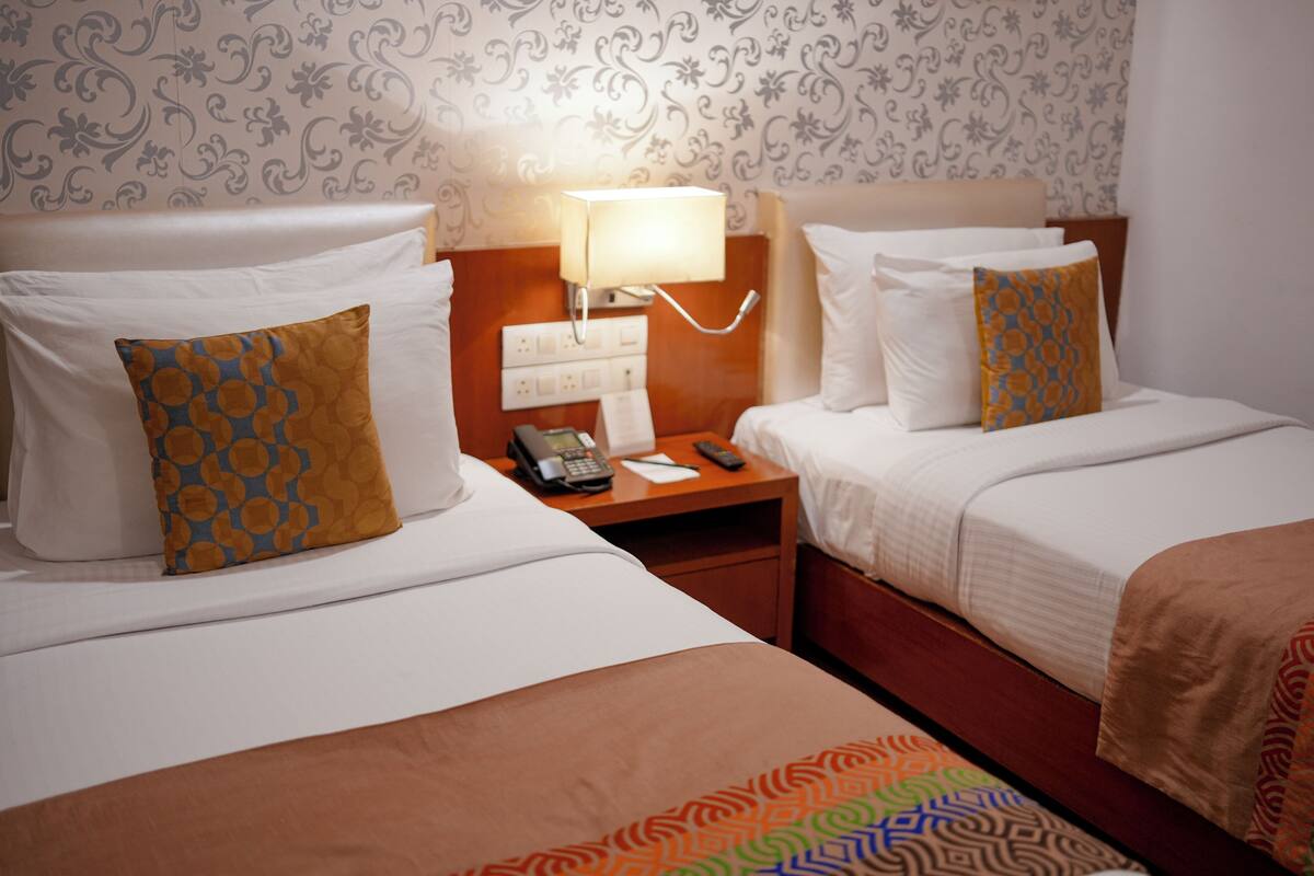 Ein Hotelzimmer mit zwei Betten, einem Nachttisch mit Lampe, Telefon und Fernbedienung.
