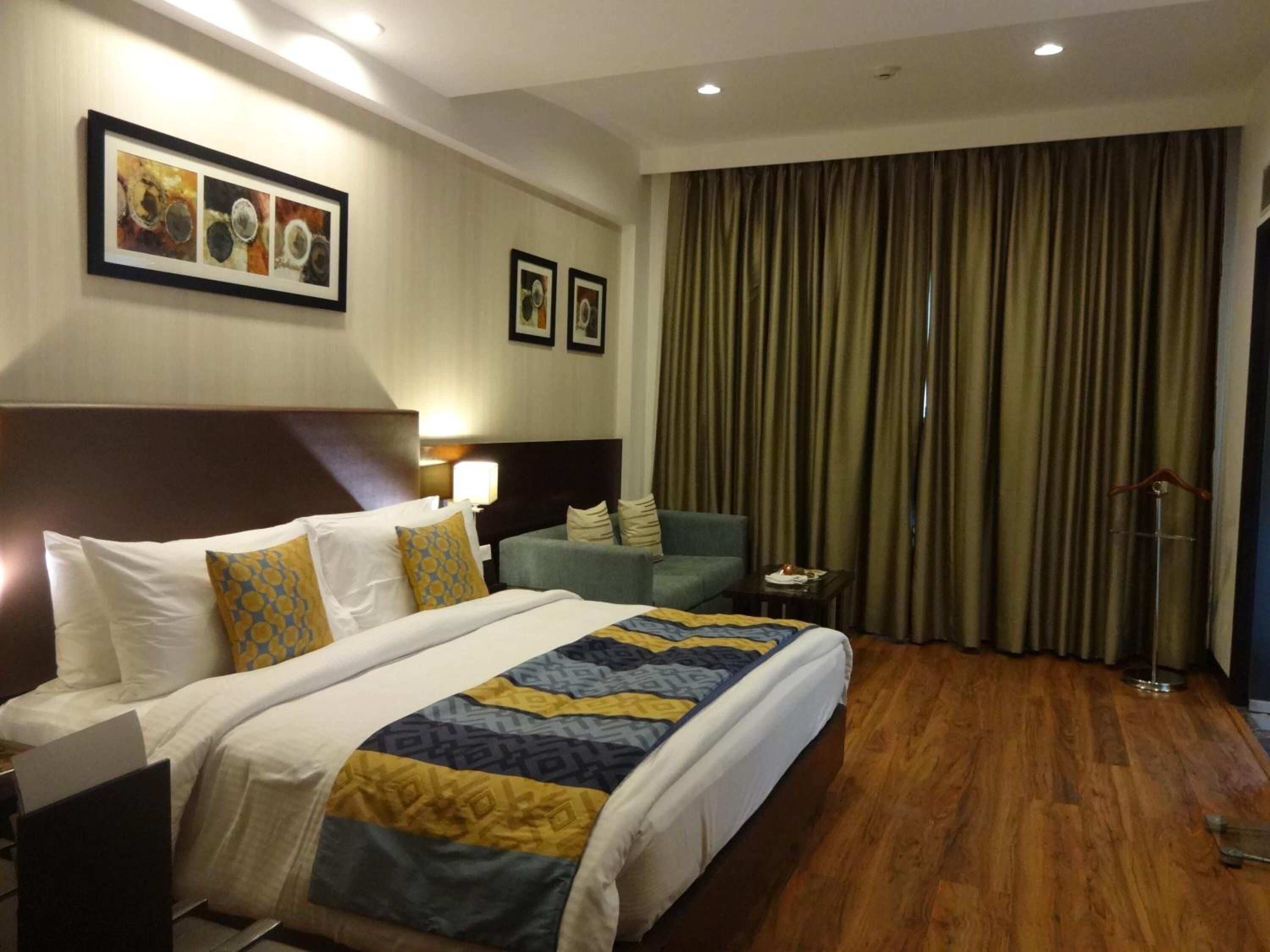 A hotel room with a large bed, a desk, a chair, a nightstand, a lamp, and a window with curtains.