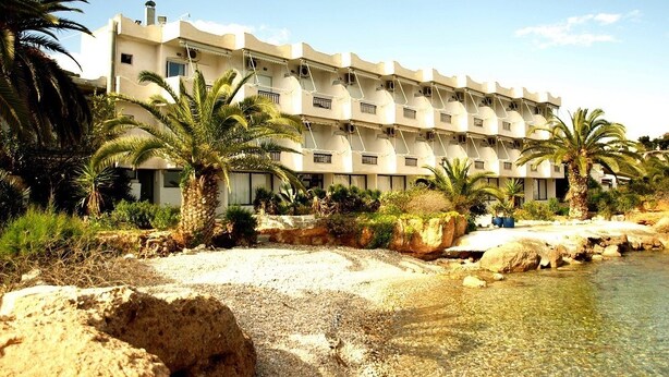 A multi-story hotel with a flat roof, palm trees, and a clear pool.