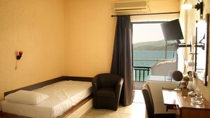 A hotel room with a bed, a desk, a chair, and a view of the sea.