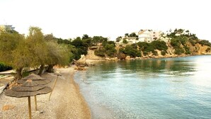 A pebble beach with umbrellas, clear water, and buildings on a hillside.