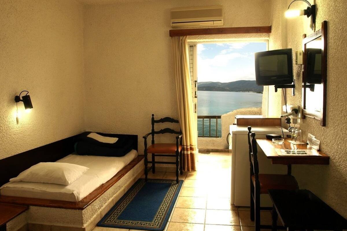 A hotel room with a bed, a desk, a chair, a TV, and a view of the sea.