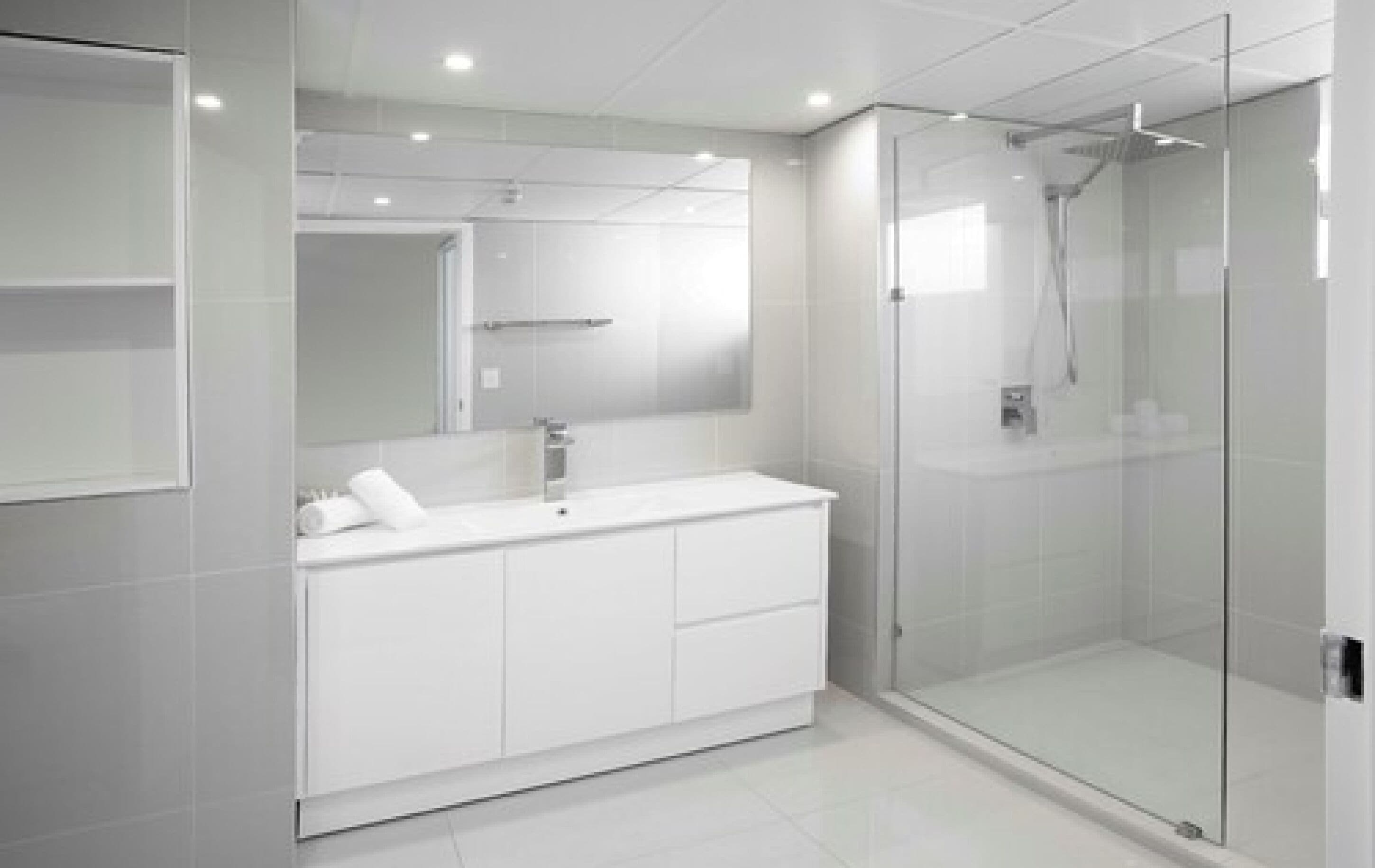 Een moderne badkamer met een douchecabine van glas, een wit wastafelmeubel met spiegel, en een betegelde vloer.