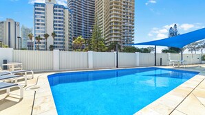 Piscina cercada por um muro branco, com espreguiçadeiras e um toldo azul.
