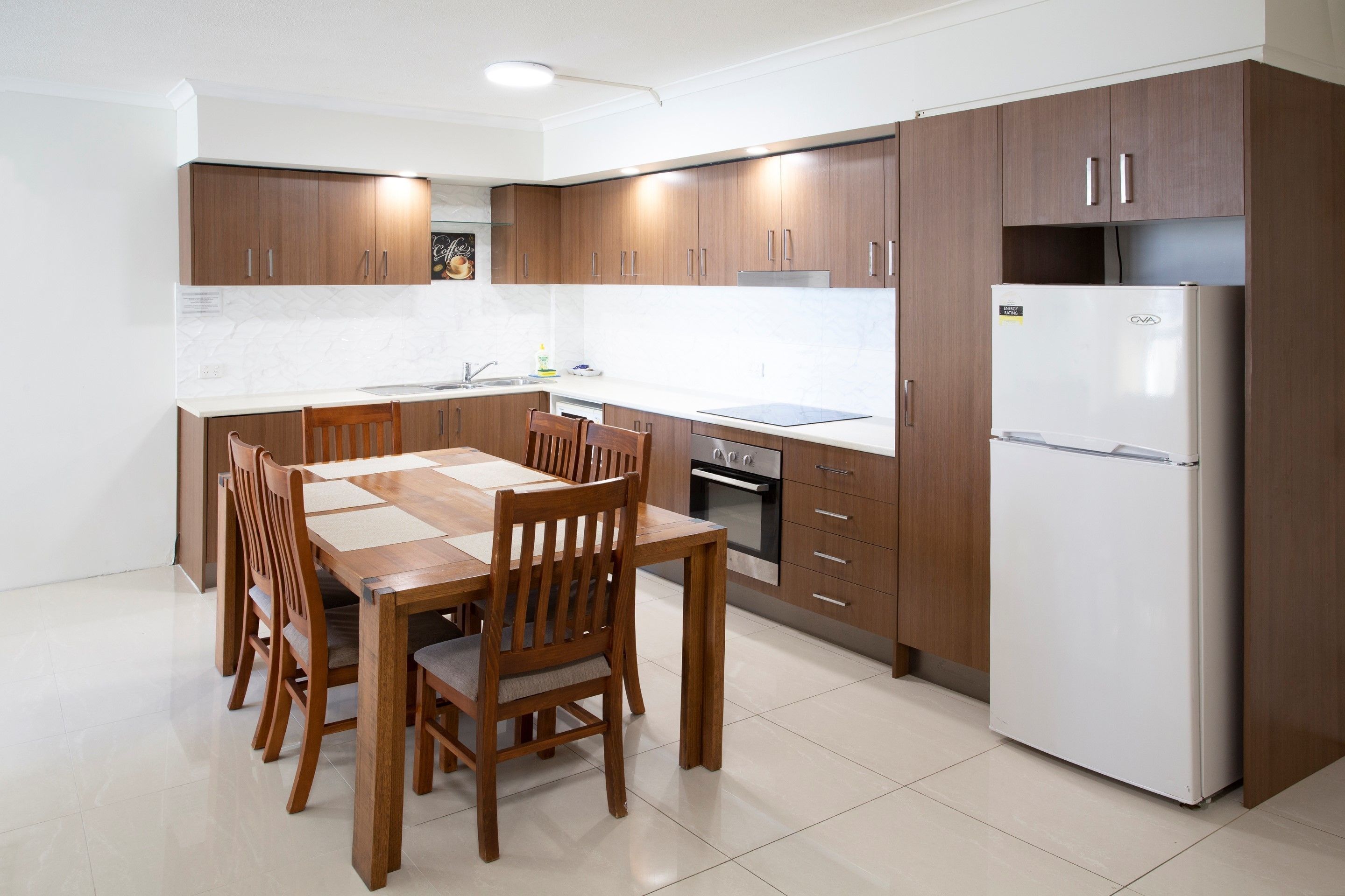 Une cuisine moderne avec des meubles en bois, un réfrigérateur en acier inoxydable et une table à manger avec des chaises.
