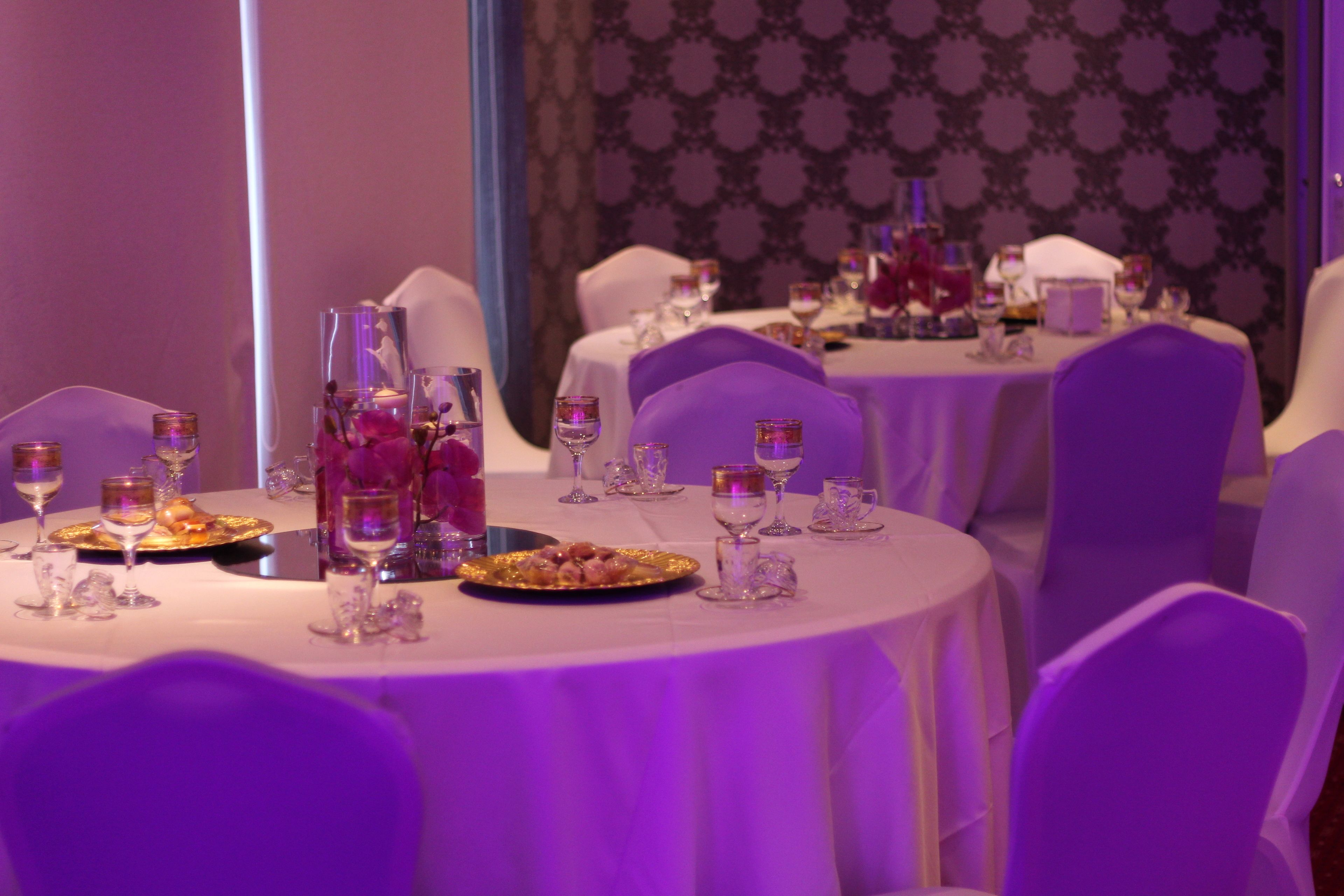 Un espace repas avec des tables rondes, des nappes blanches et des chaises violettes.