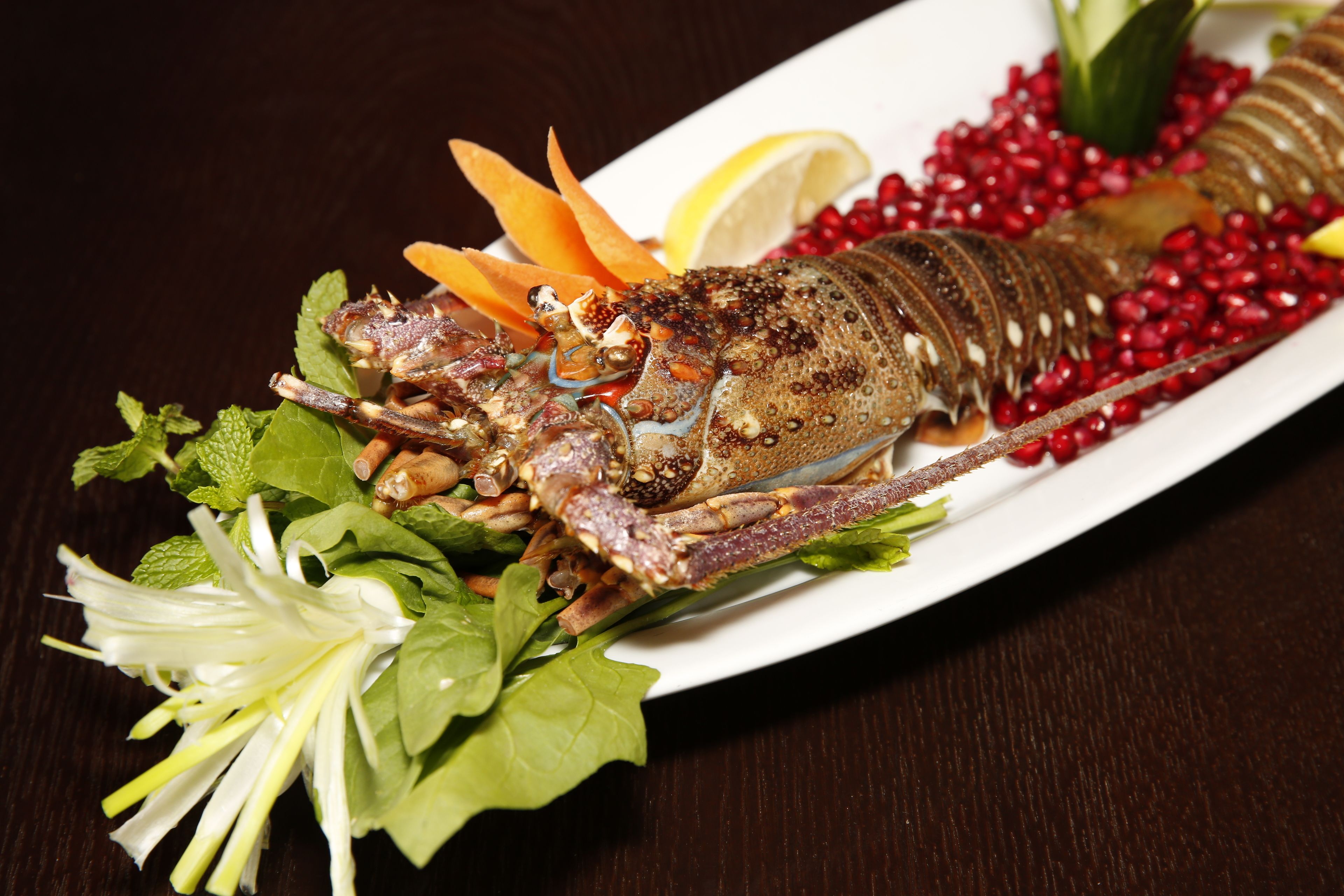 A lobster dish with garnishes and a white plate on a dark wooden table.