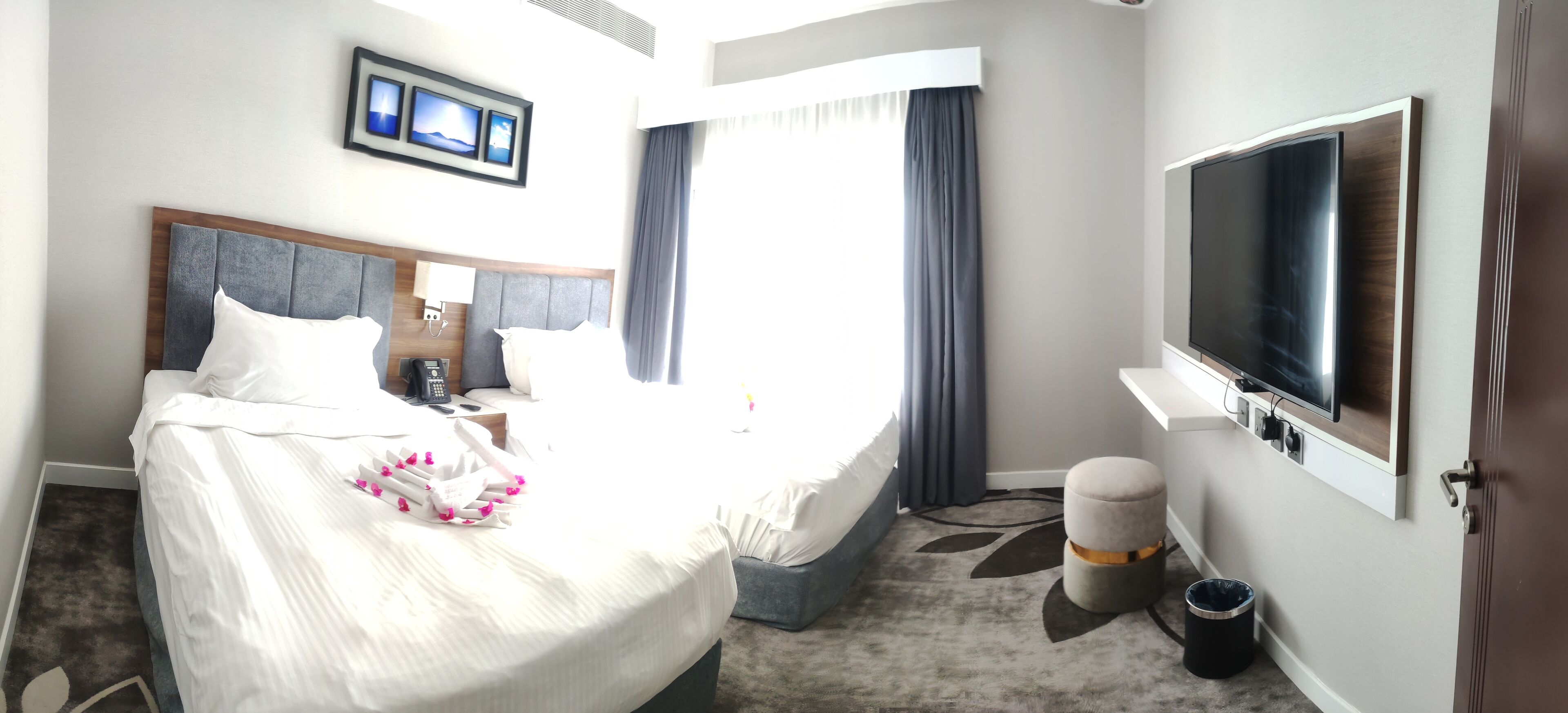 A hotel room with a bed, a TV, a desk with a lamp, a phone, and a window with curtains.
