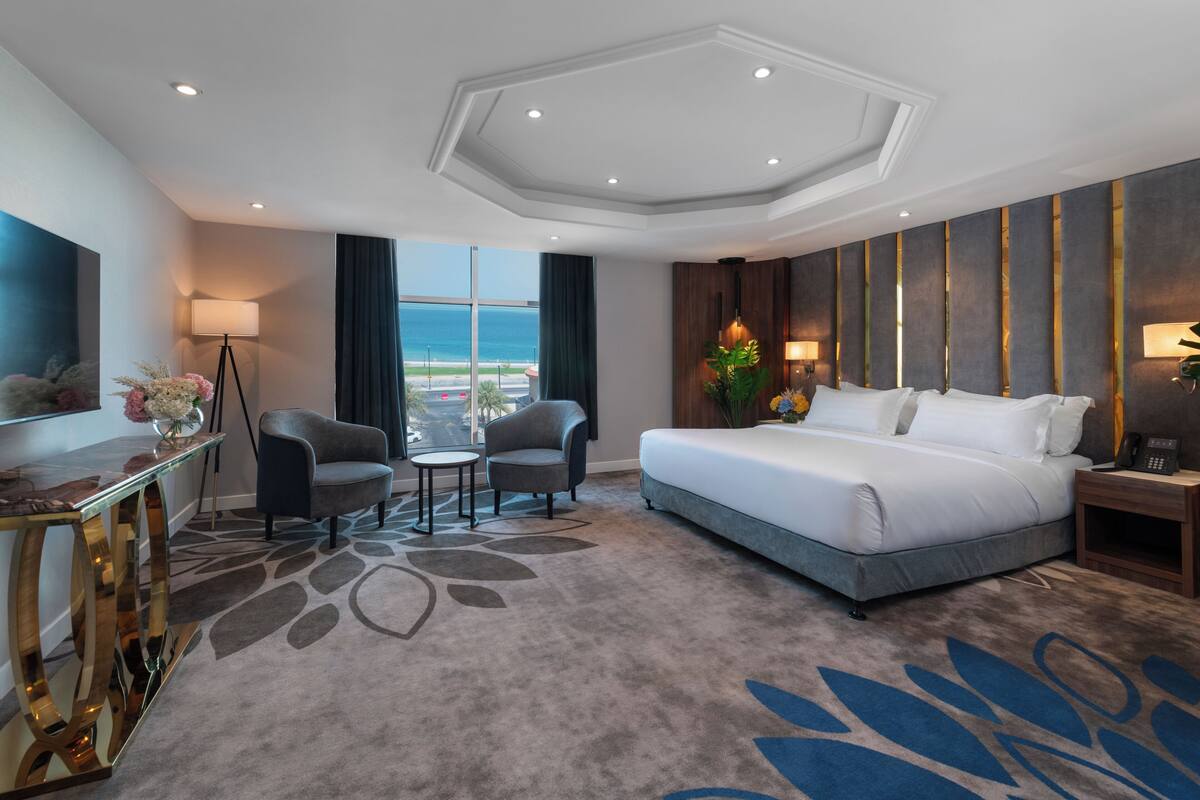 A hotel room with a large bed, a desk, two chairs, a small table, and a view of the ocean.
