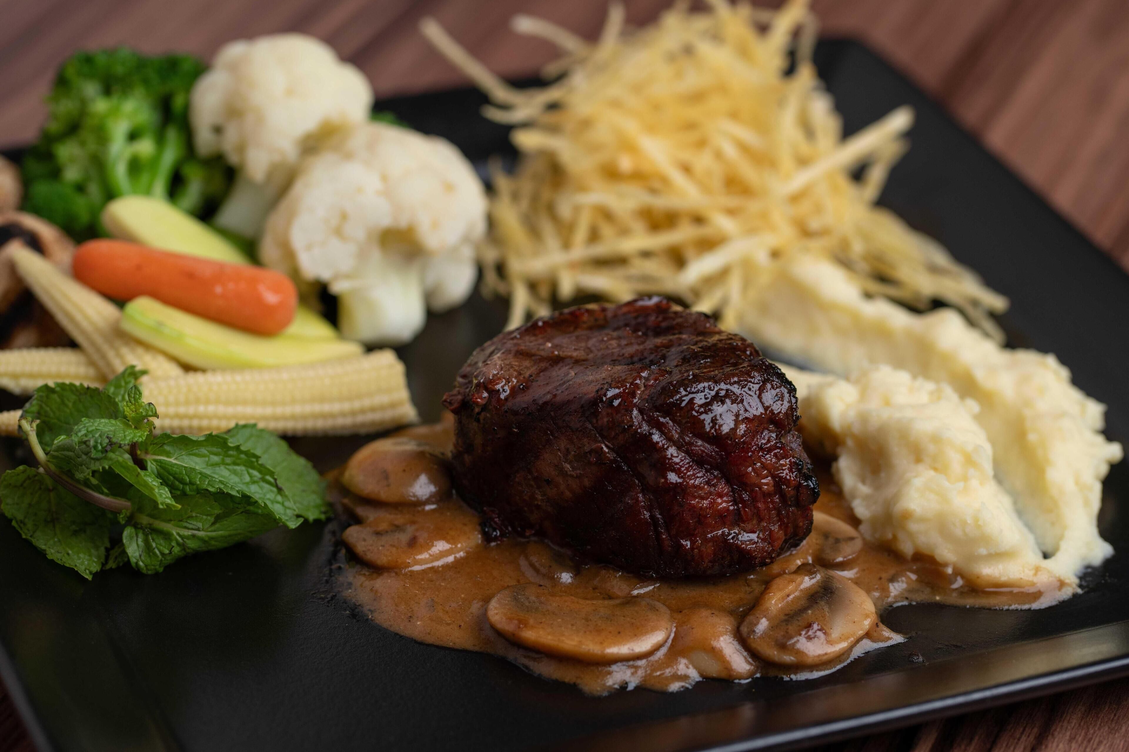 A plate with a steak, mushrooms, corn, and vegetables.