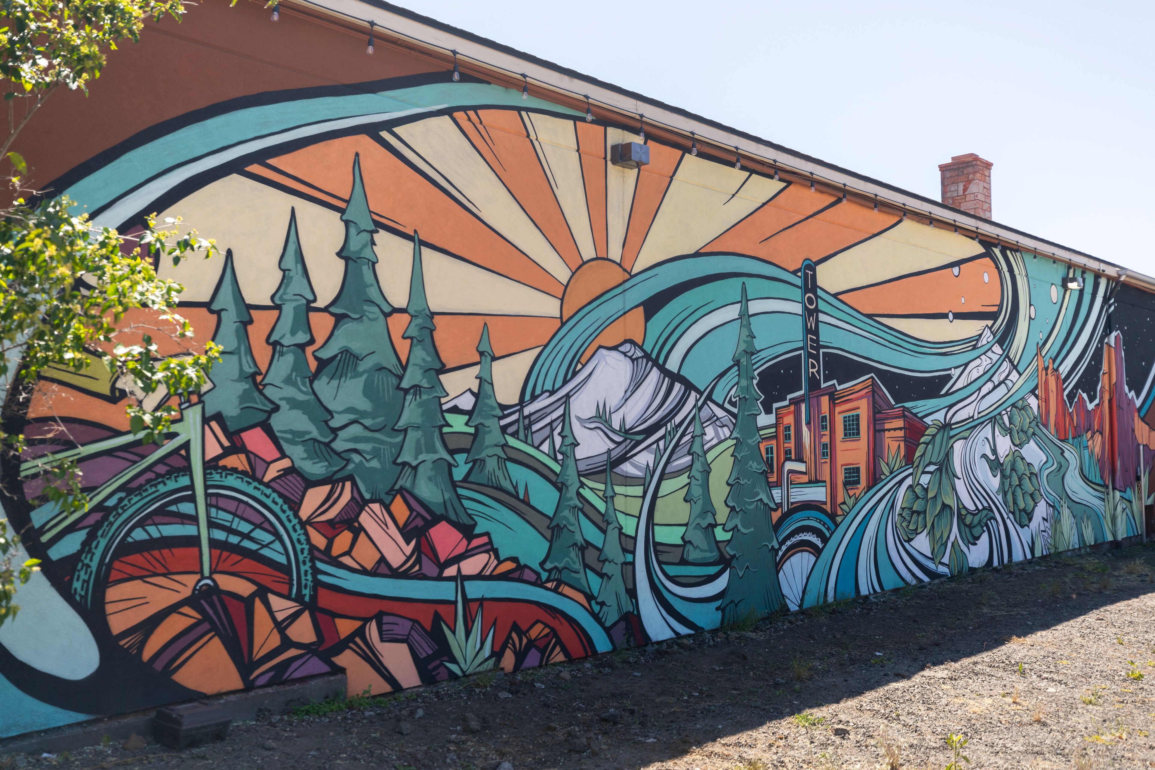A colorful mural on a building wall featuring a mountain, trees, and a house.
