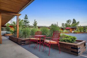 Un espace extérieur aménagé avec des chaises et une table en métal rouge, entouré de jardinières en bois et de verdure.
