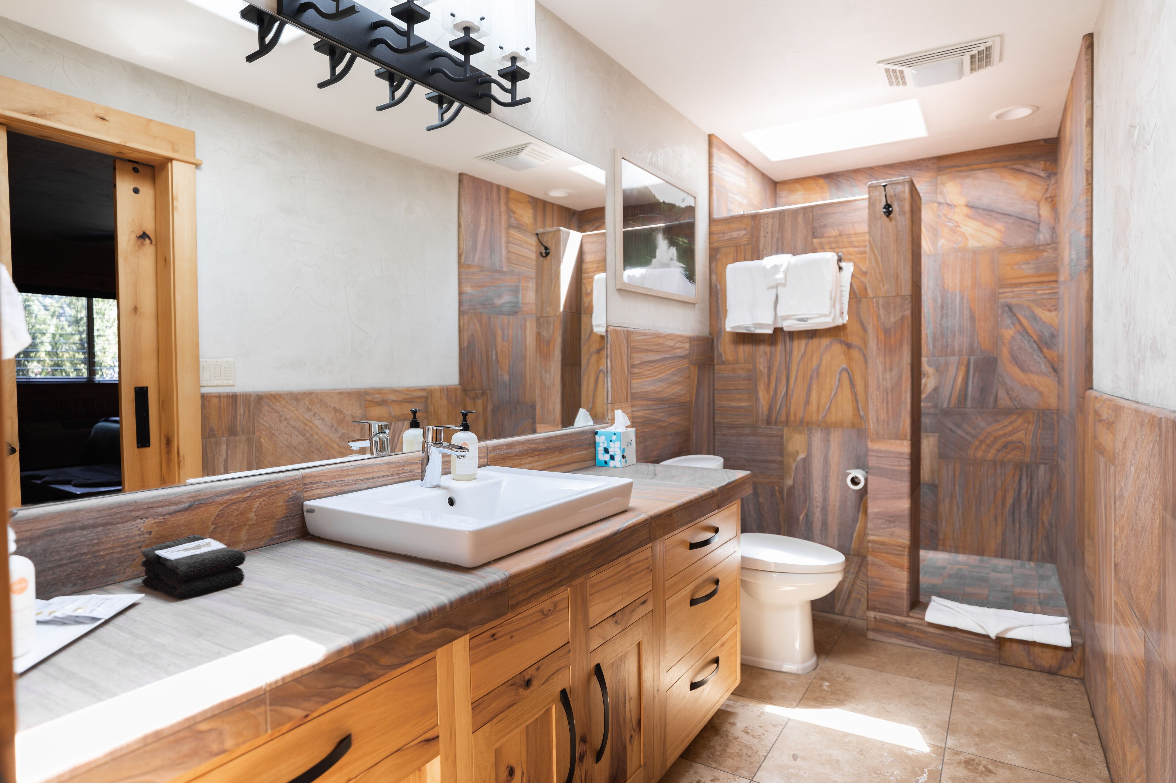 Een moderne badkamer met een houten wastafelmeubel, een grote spiegel, een douchecabine en een toilet.