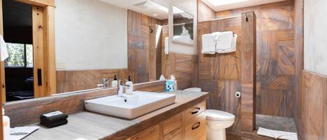 Een moderne badkamer met een houten wastafelmeubel, een grote spiegel, een douchecabine en een toilet.