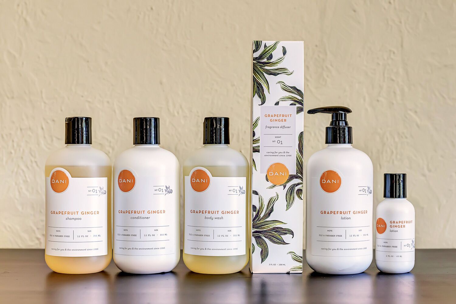 Colección de artículos de aseo Dani, incluyendo champú, acondicionador, gel de baño, loción y un difusor de fragancia, todos etiquetados con 'pomelo y jengibre' y 'sin parabenos'.
