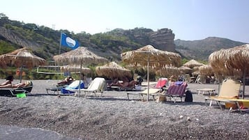 A beach with thatched umbrellas and sun loungers.