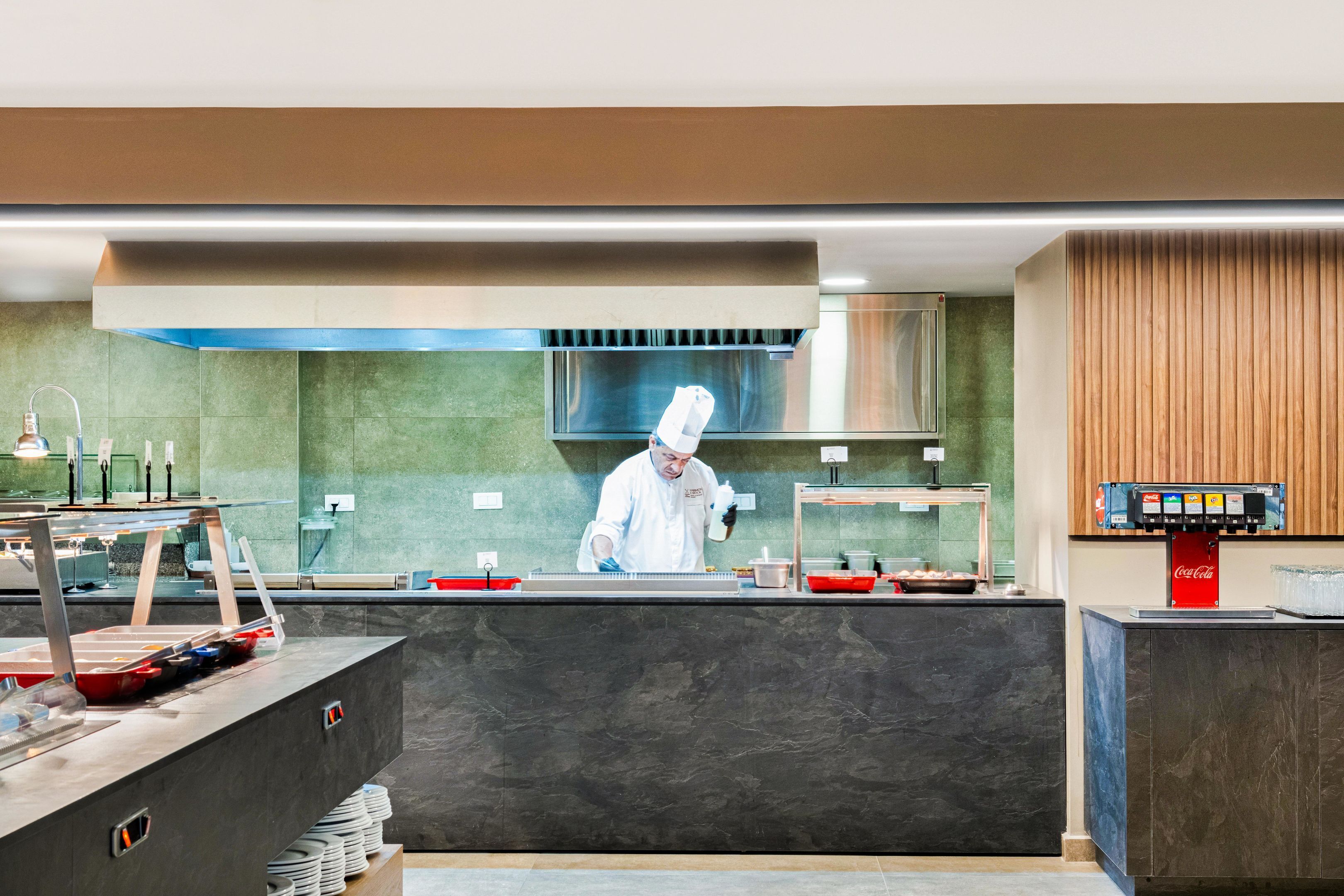 Una cocina moderna con un chef preparando comida, una cafetera y una pila de platos.