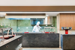 Une cuisine moderne où un chef prépare des plats, avec une machine à café et une pile d’assiettes.