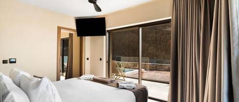 A modern hotel room with a large bed, a ceiling fan, a flat-screen TV, and a view of a swimming pool.