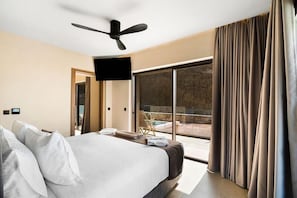 A modern hotel room with a large bed, a ceiling fan, a flat-screen TV, and a view of a swimming pool. - Harmony E Rock Hotel (Ierapetra)