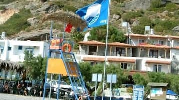 A beach area with a lifeguard tower, a flag, and buildings in the background.