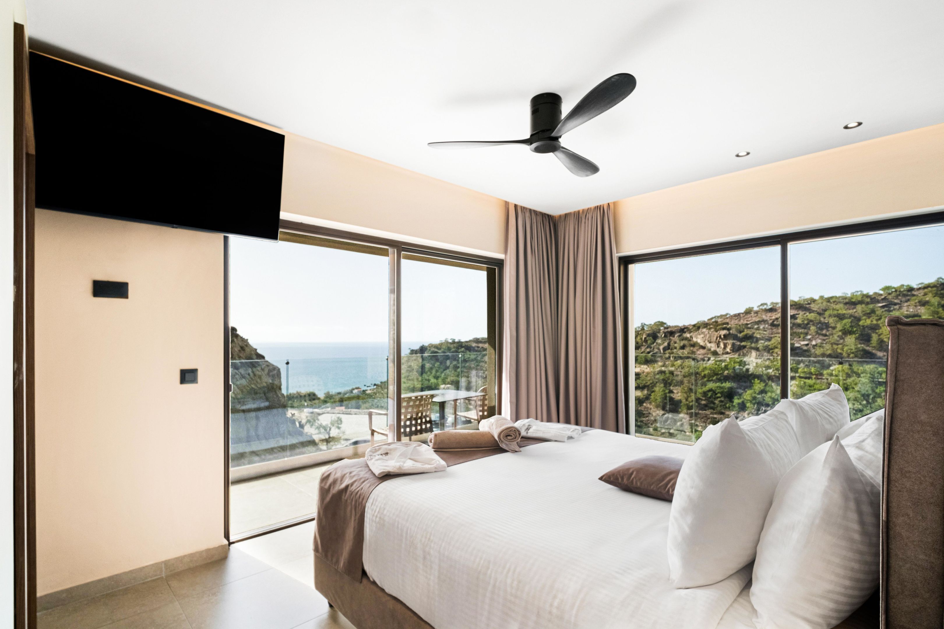 Ein modernes Hotelzimmer mit einem großen Bett, einem Deckenventilator und Meerblick.