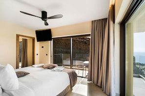 A hotel room with a large bed, a ceiling fan, a TV, and a balcony with curtains. - Harmony E Rock Hotel (Ierapetra)
