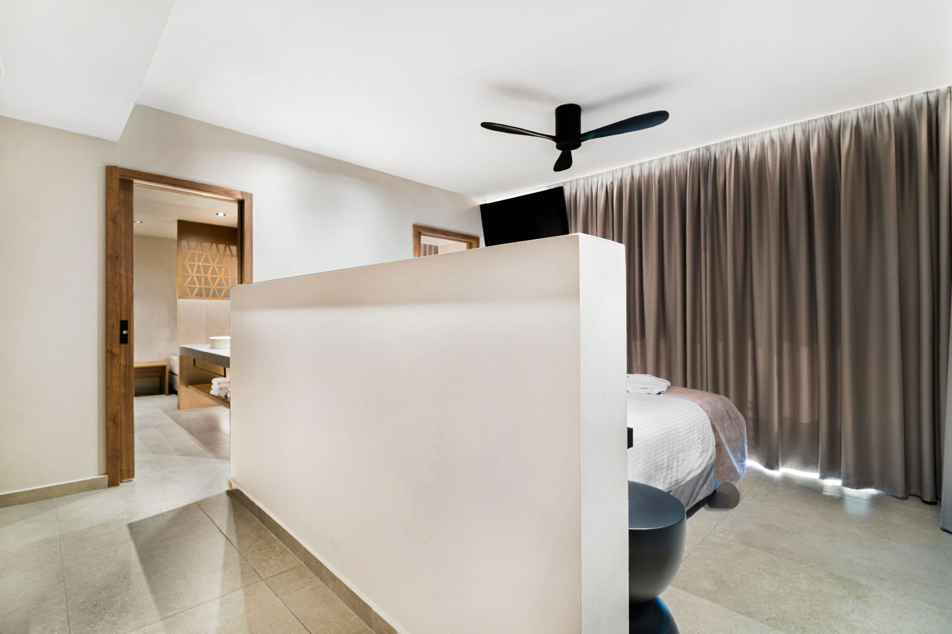 A modern hotel room with a large bed, a desk, and a ceiling fan.
