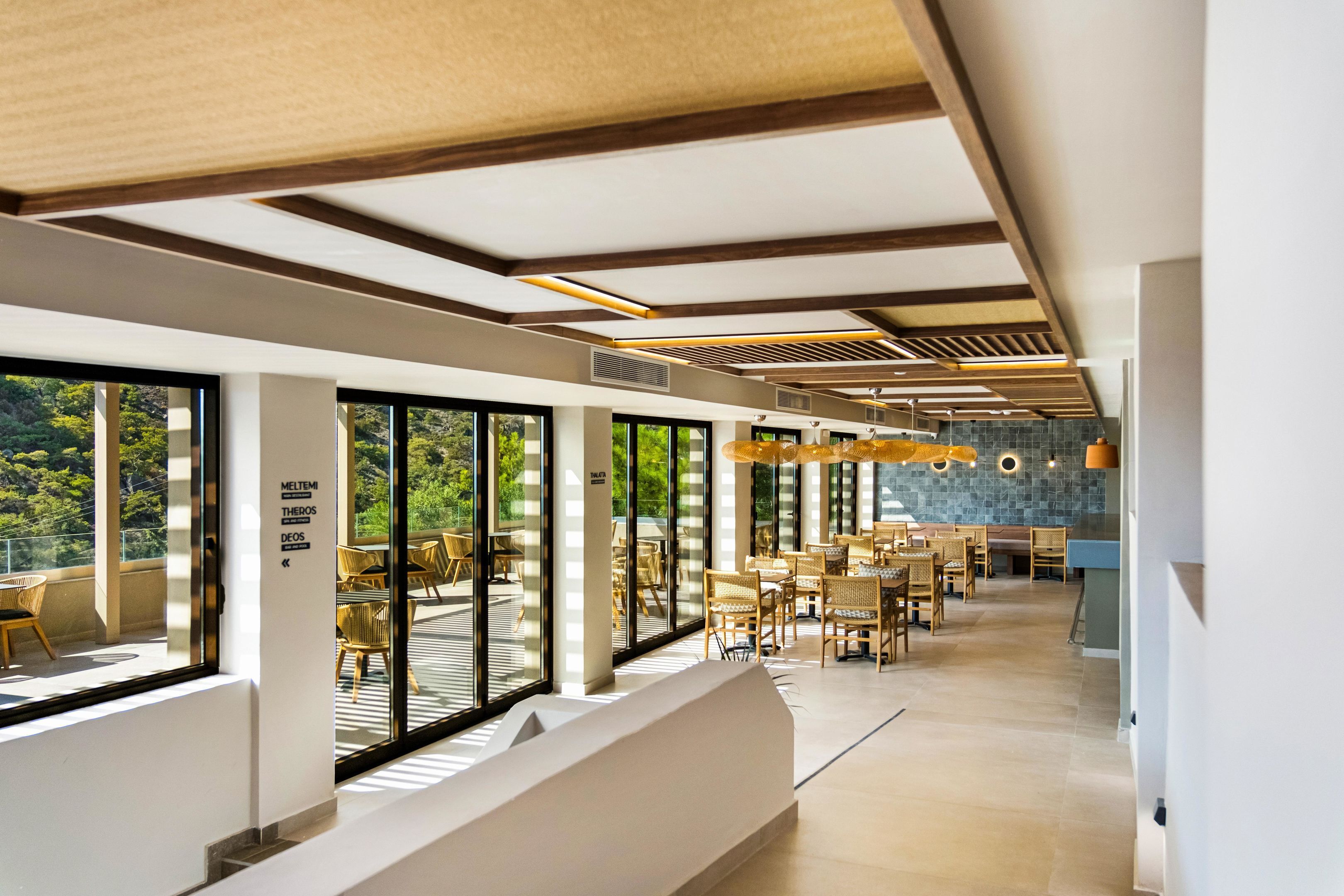 Un intérieur moderne avec de grandes fenêtres, des poutres en bois au plafond et un coin repas doté de meubles en osier.