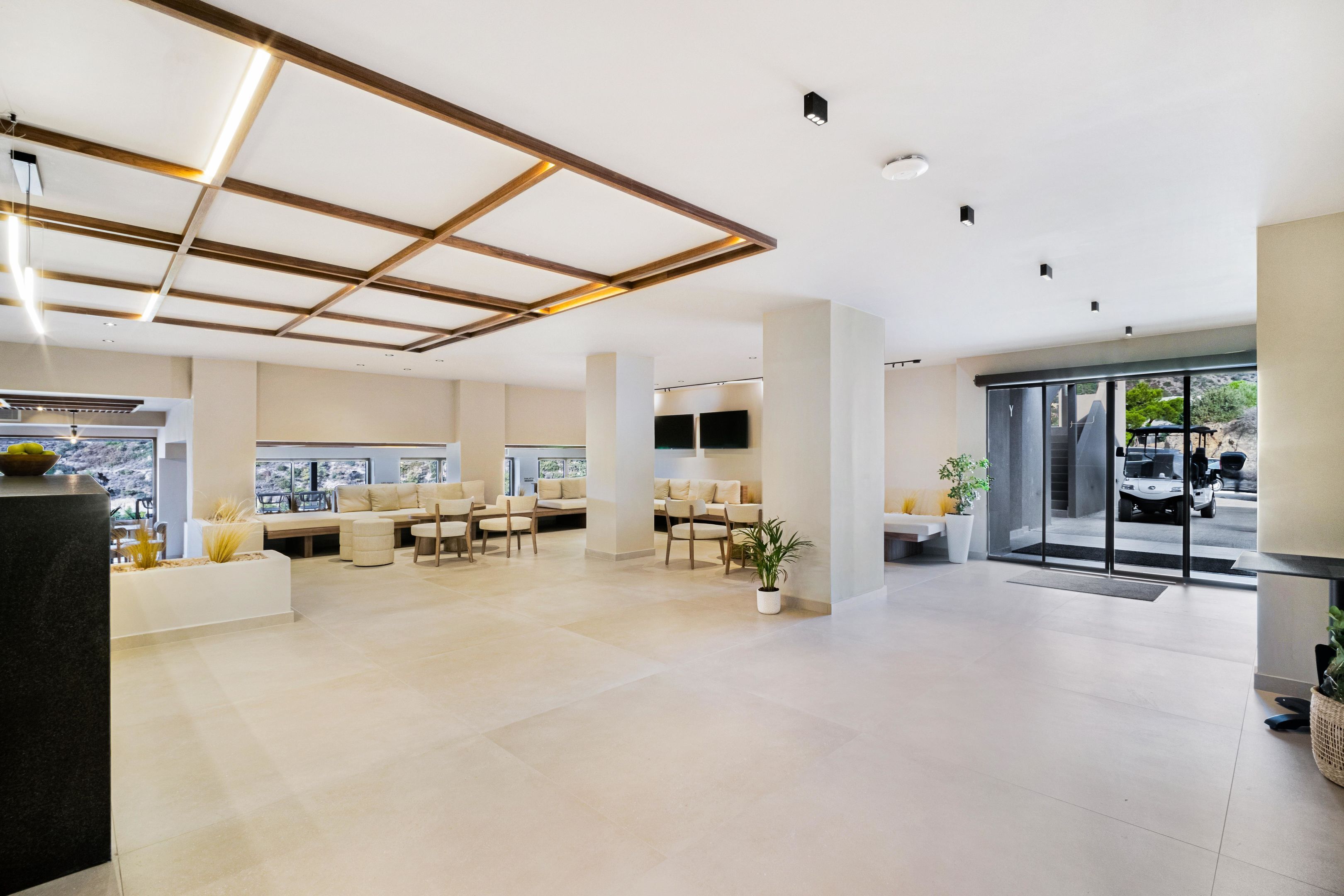 A spacious lobby with a modern design, featuring a seating area with sofas and chairs, a reception desk, and large windows offering a view of the outside.