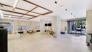A spacious lobby with a modern design, featuring a seating area with sofas and chairs, a reception desk, and large windows offering a view of the outside.
