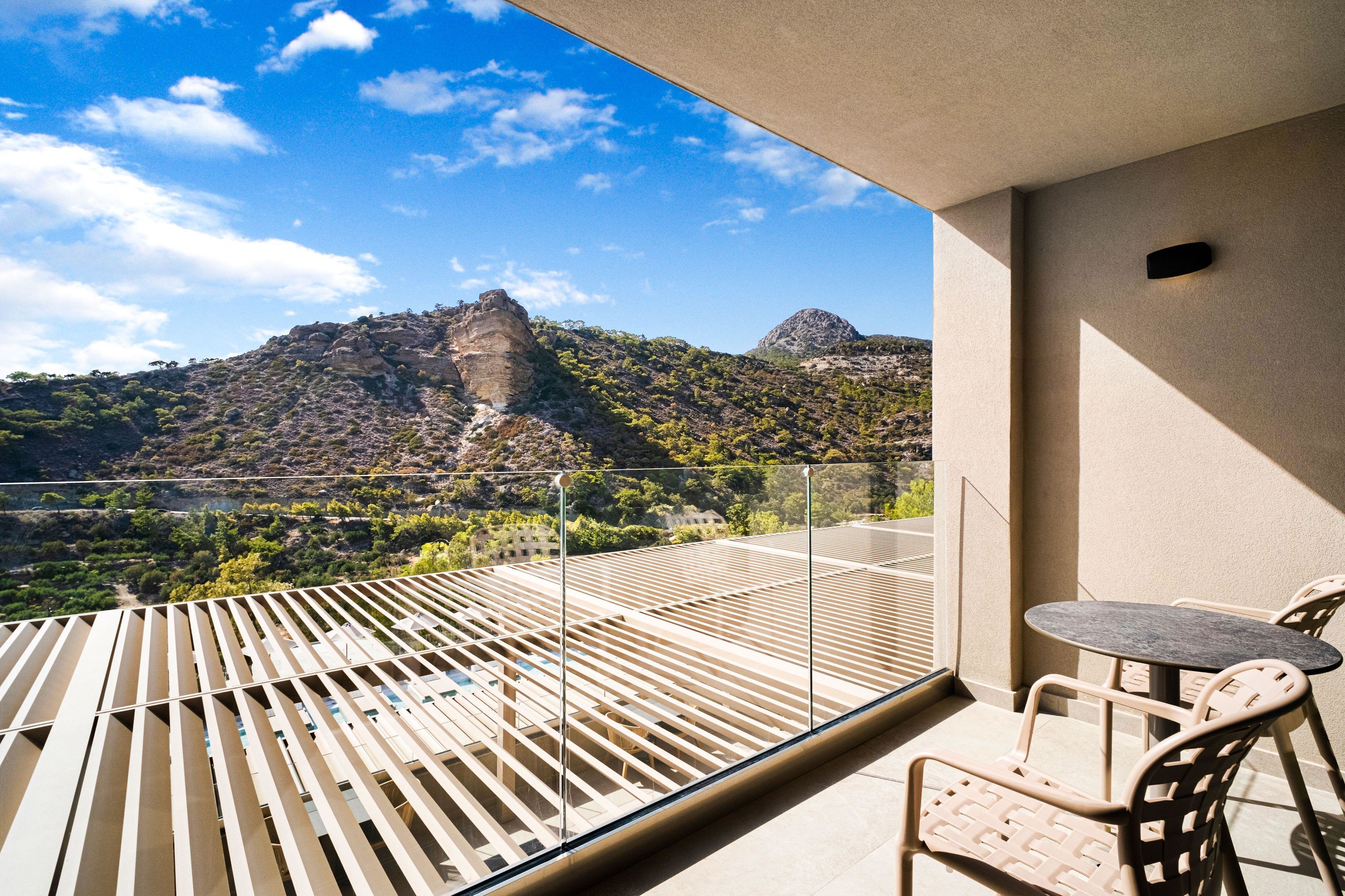 A balcony with a table and chairs, overlooking a mountainous landscape.