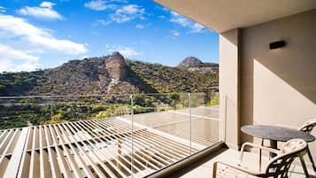A balcony with a table and chairs, overlooking a mountainous landscape.