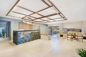 En modern hotellobby med en receptionsdisk, en sittgrupp och utsikt över omgivningarna.