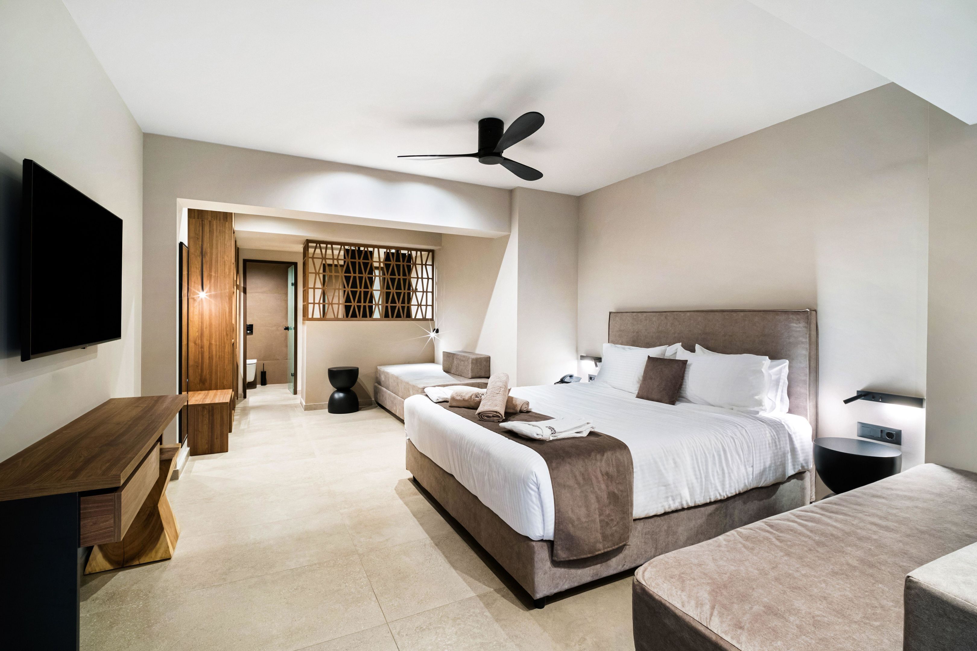 A modern bedroom with a large bed, bedside tables, a TV, and a ceiling fan.