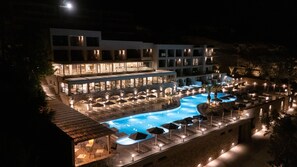 A nighttime view of a hotel with a swimming pool, outdoor seating, and multiple dining areas. - Harmony E Rock Hotel (Ierapetra)