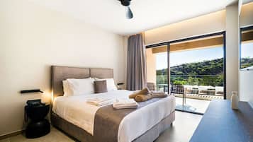 A modern hotel room with a large bed, a ceiling fan, a balcony with a view of the hills, and a desk with a vase.