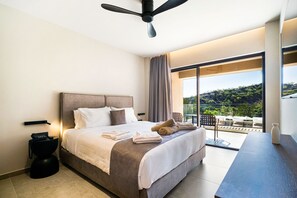 Ett modernt hotellrum med en stor säng, en takfläkt, en balkong med utsikt över kullarna och ett skrivbord med en vas.