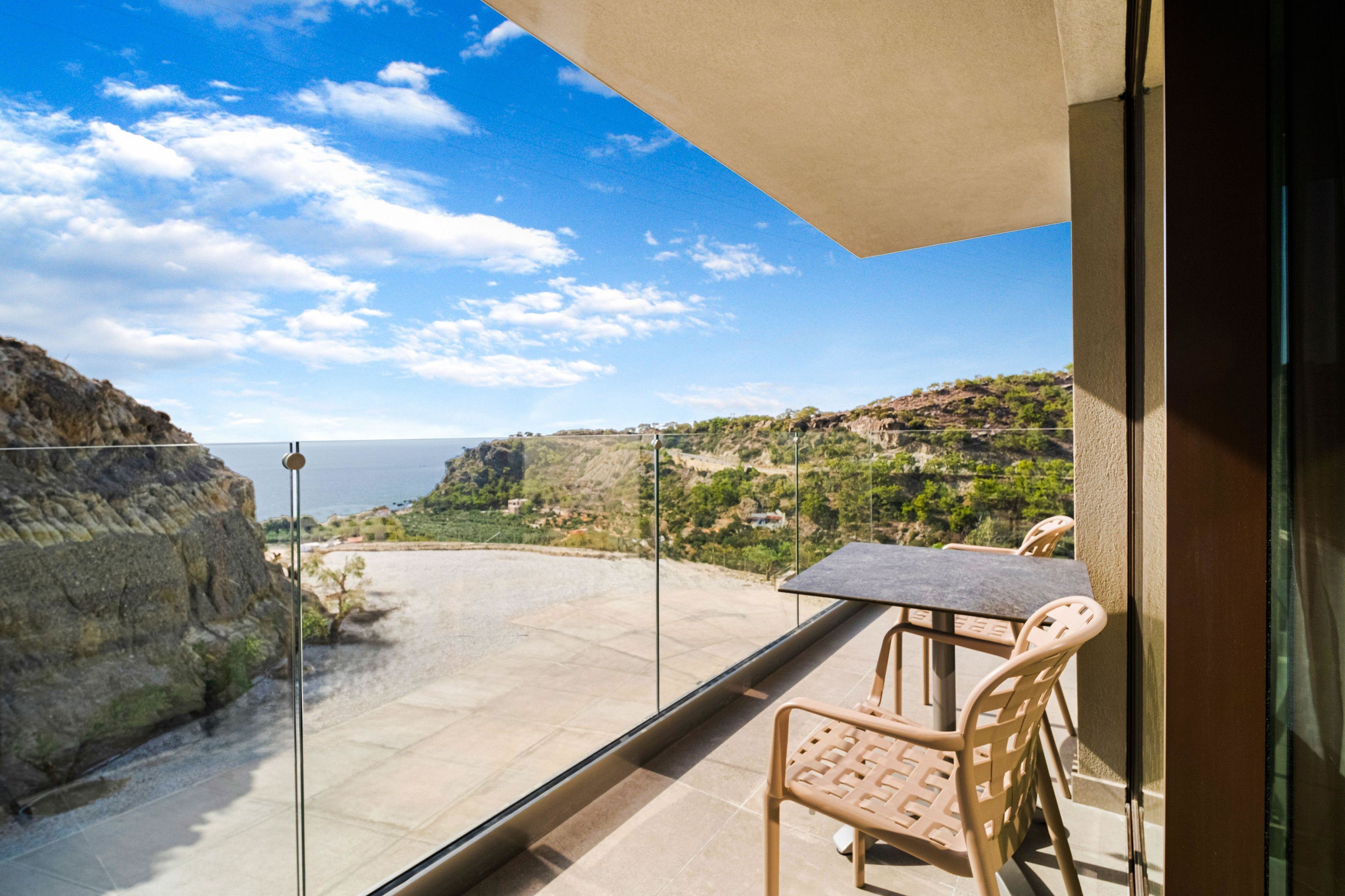 A balcony with a table and chairs overlooking a coastal landscape.