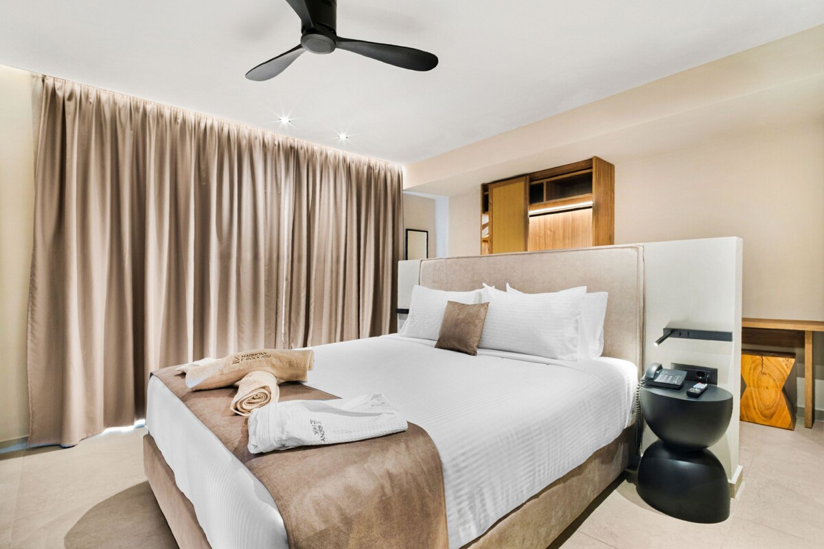 Een moderne hotelkamer met een groot bed, een plafondventilator, een nachtkastje met telefoon en een houten kast.