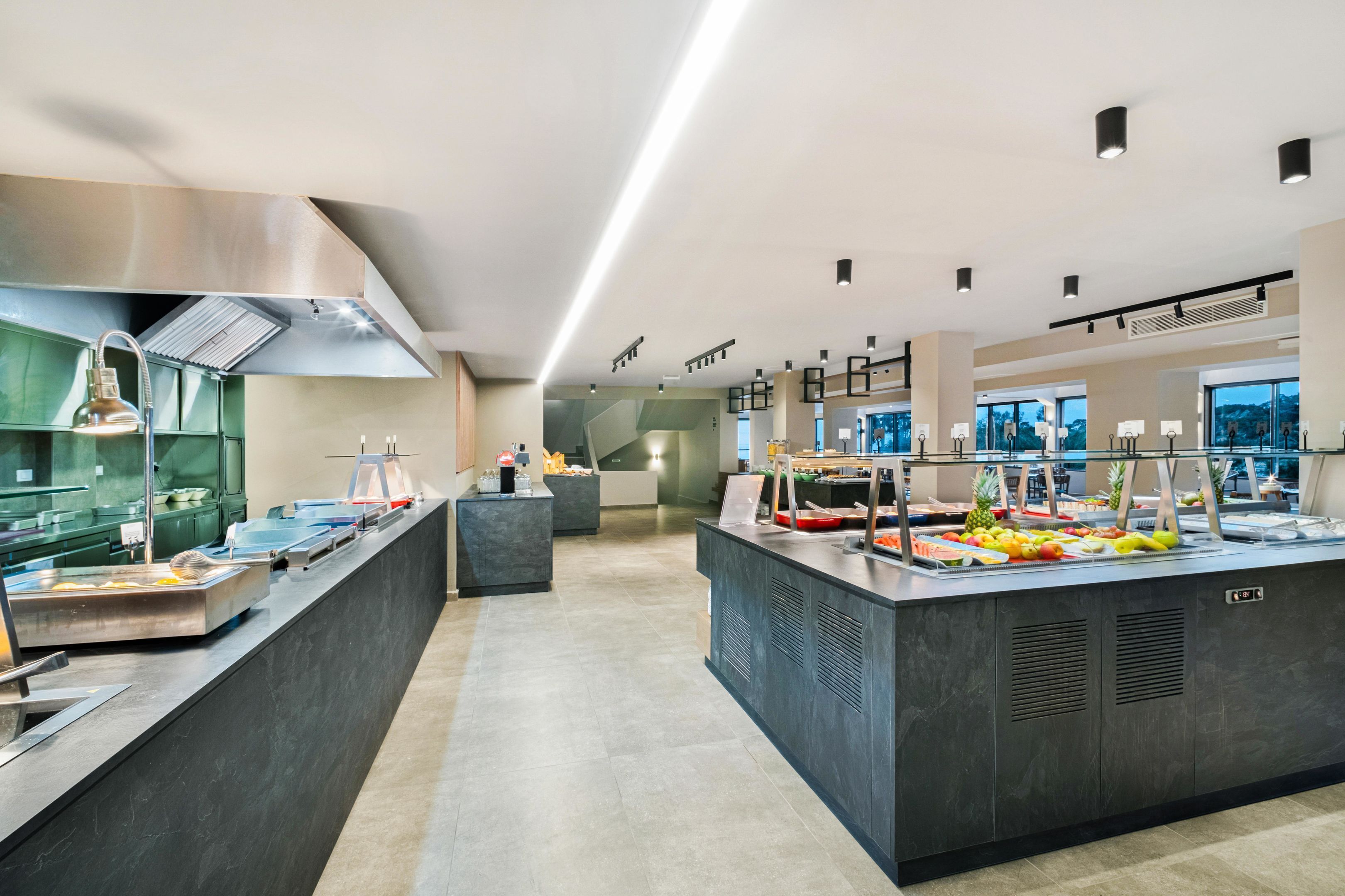 Un área de buffet moderna con diversas opciones de comida, una campana extractora de acero inoxidable y un ambiente limpio y bien iluminado.
