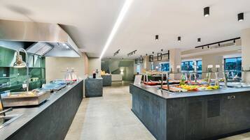 Un área de buffet moderna con diversas opciones de comida, una campana extractora de acero inoxidable y un ambiente limpio y bien iluminado.