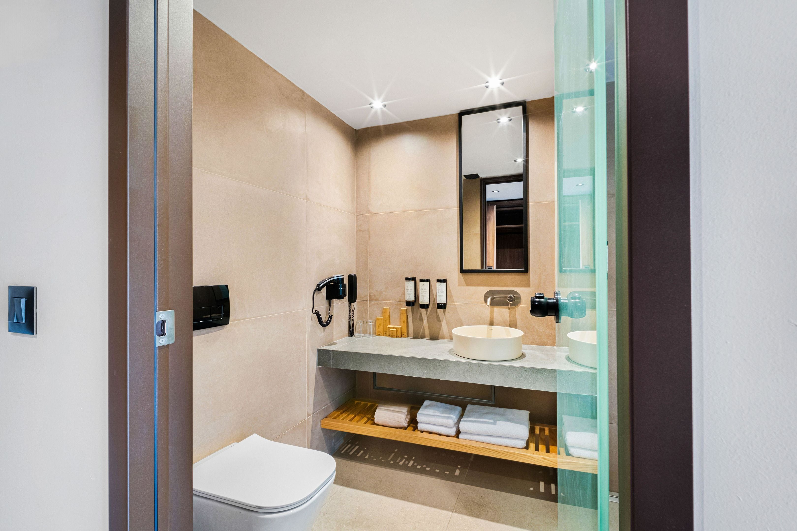 Un baño moderno con inodoro, lavabo y espejo. Hay toallas y artículos de aseo en la encimera.