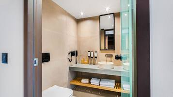 Un baño moderno con inodoro, lavabo y espejo. Hay toallas y artículos de aseo en la encimera.