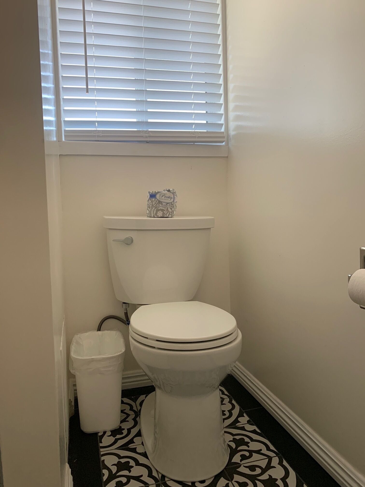 Un baño pequeño con inodoro, un bote de basura y una ventana con persianas.