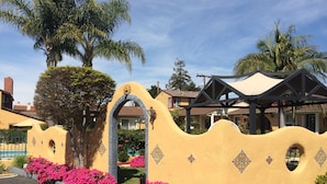 A building with a distinctive wavy facade, a decorative archway, and vibrant pink flowers in the foreground. - Oasis Inn & Suites (Santa Barbara)