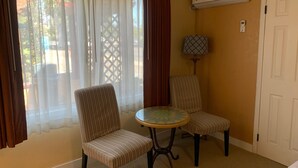 A room with two striped chairs, a small round table, and an air conditioning unit on the wall. - Oasis Inn & Suites (Santa Barbara)