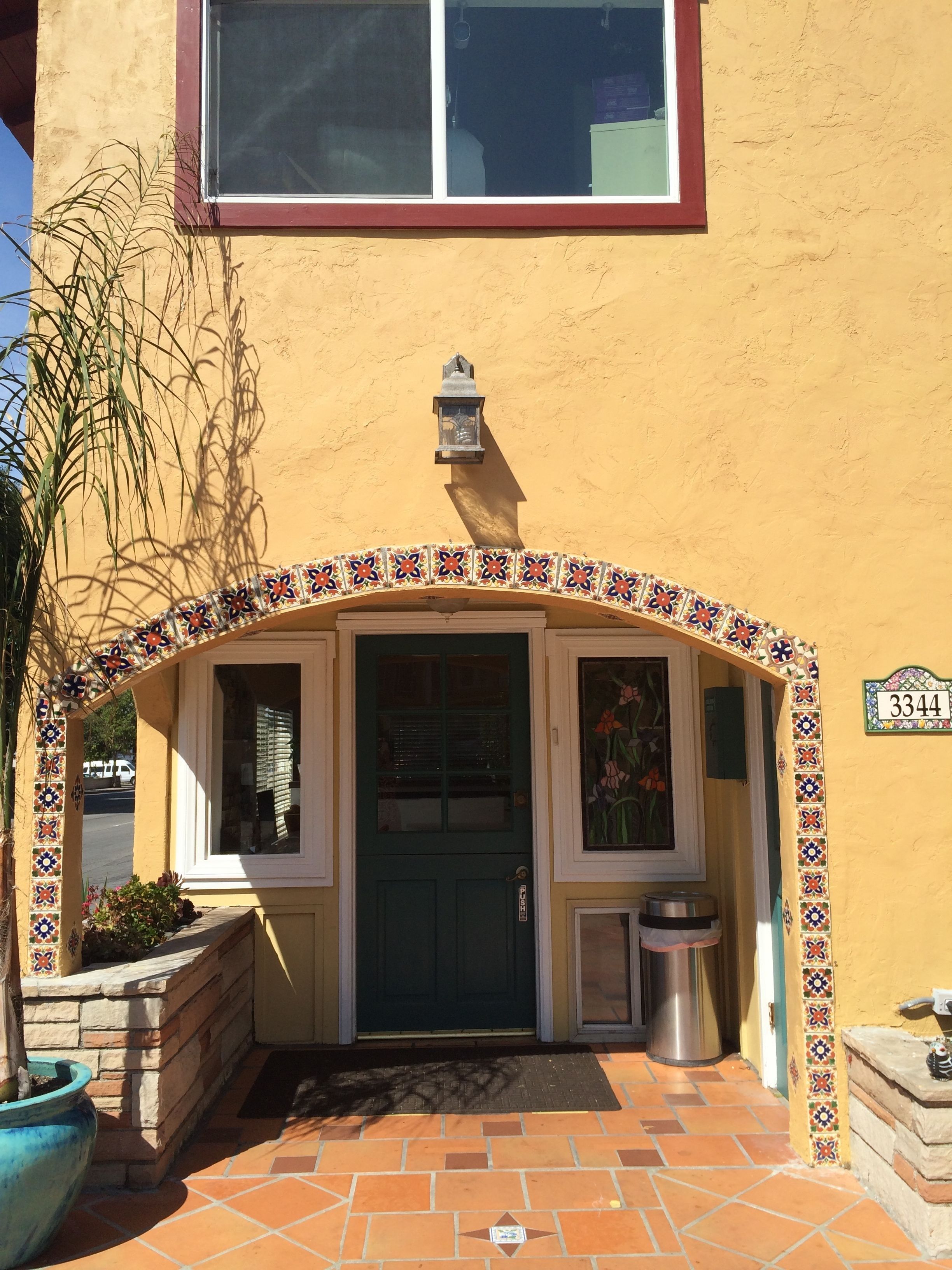 A building with a tiled entrance, a green door, and a number sign "3344".