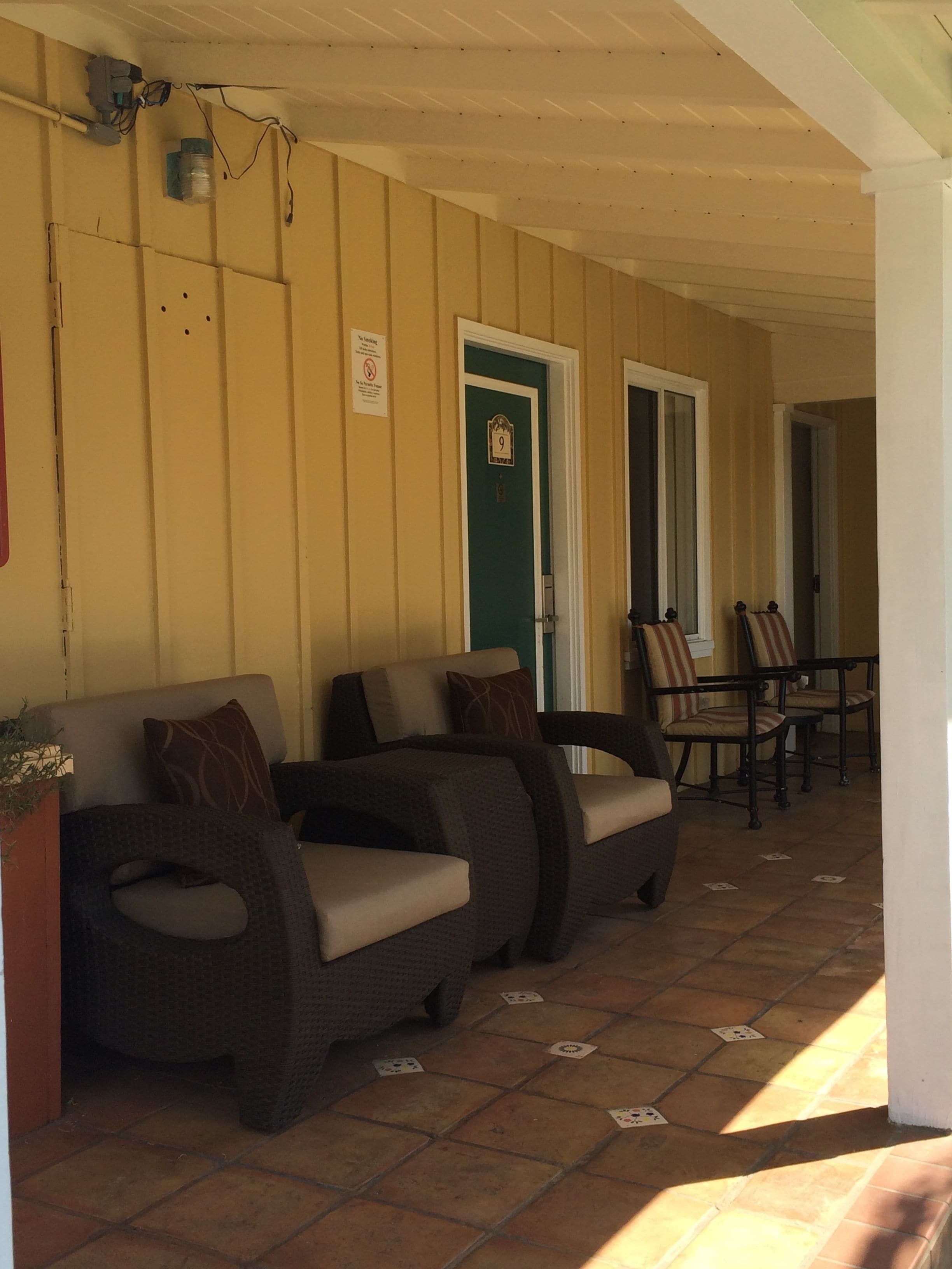 A covered porch with two sofas and chairs, a door with the number 9, and a sign prohibiting smoking.